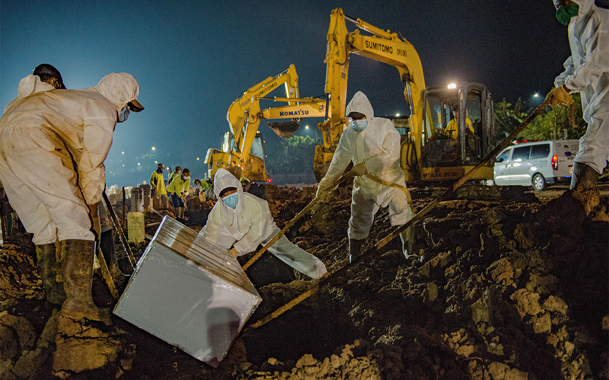 Gravediggers in Jakarta, Indonesia, wearing personal protective equipment to bury a victim of Covid-19, 6 July 2021 (photograph by Medialys Images by Massimiliano Ferraro / Alamy)